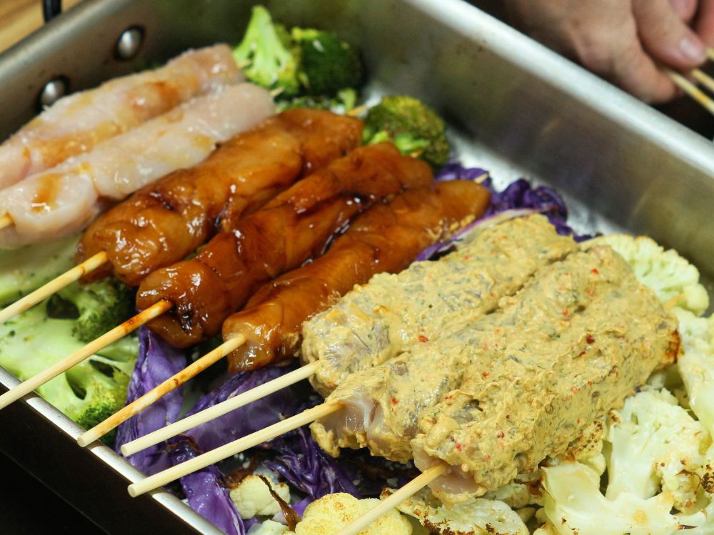 raw chicken kebabs on vegetables in a roasting tray